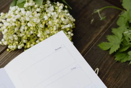A handy weekly planner featured in this image, set on a desk surrounded by beautiful flowers, perfect for organizing your schedule.
