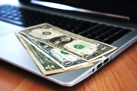 A laptop with dollar bills, indicating an easy side hustle for extra income.